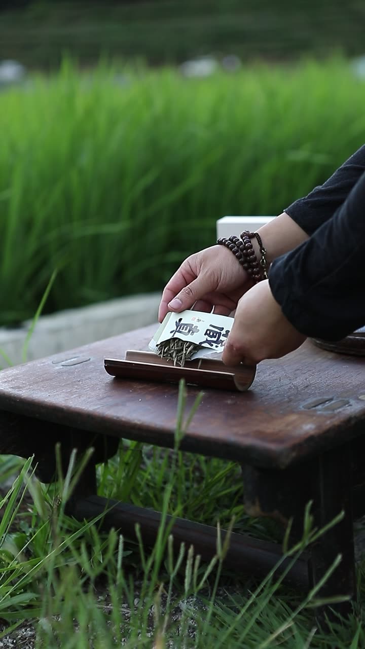 Opening a packet of withered leaf at a low table in the fields