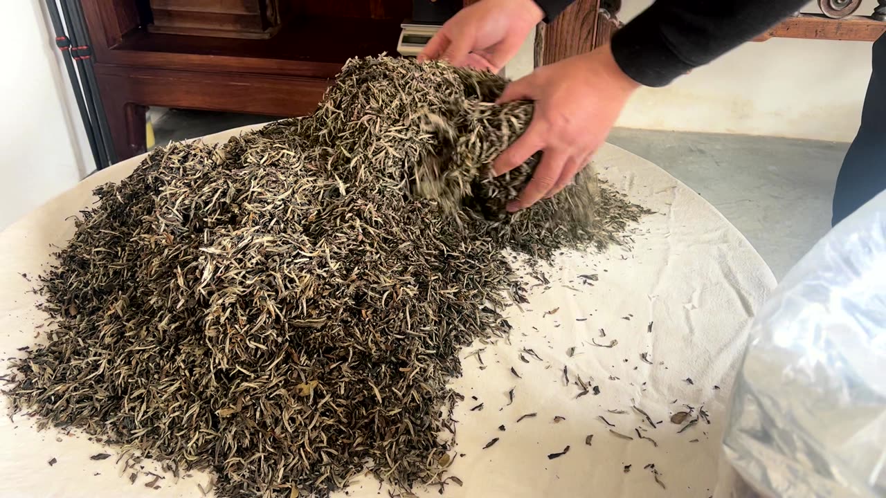 Hands turning silver needle in a bamboo tray